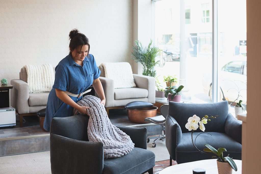 Aurora Spa 15 image of Greta, an interior designer in Minneapolis, for Tiffany Hanken Design, placing a chunky knit throw blanket over a chair