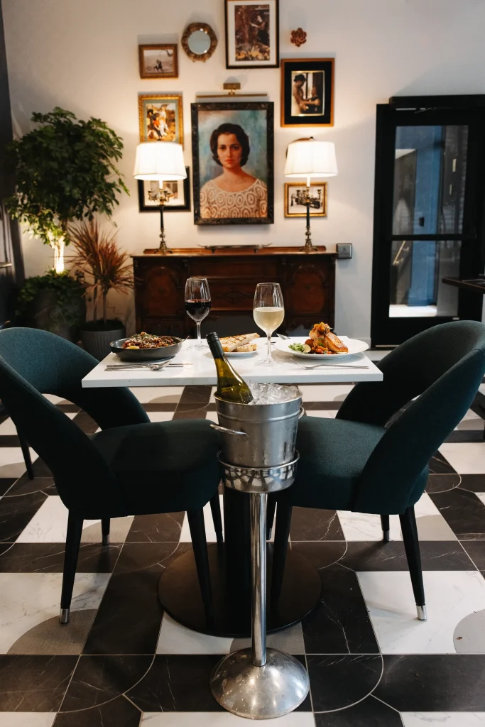 Esther's Table: Bringing a Legendary Minneapolis Hostess Back to the Table 7 Table set for two with wine and entrées beneath a portrait of Esther Capp and an antique sideboard at Esther's Table
