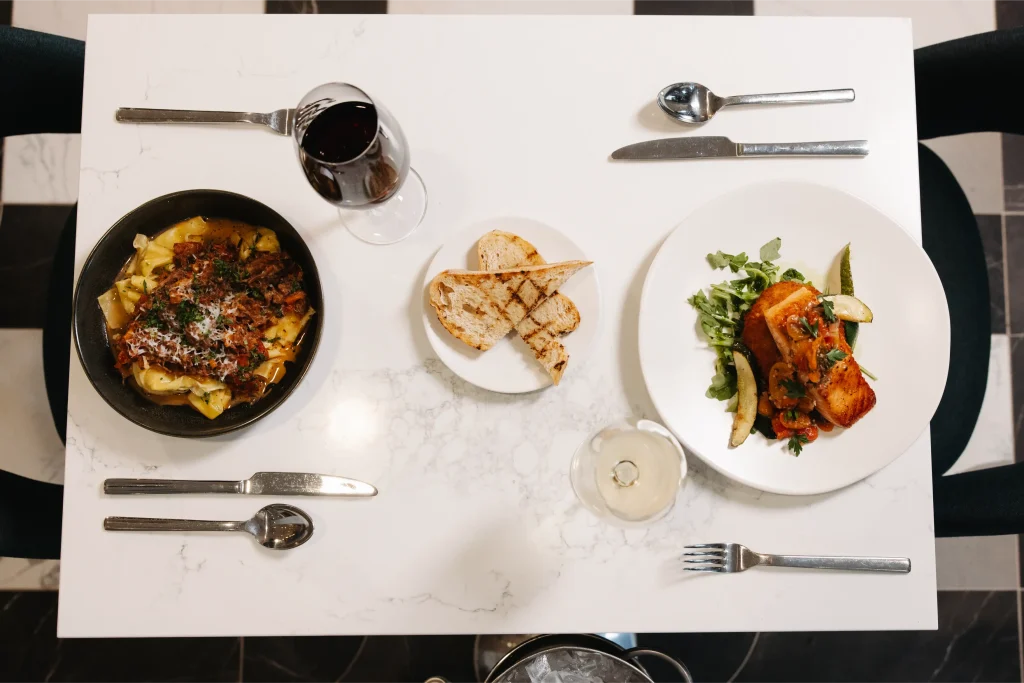 Esther's Table: Bringing a Legendary Minneapolis Hostess Back to the Table 23 Overhead view of a marble table at Esther's Table with braised pasta, seared salmon, grilled bread and wine