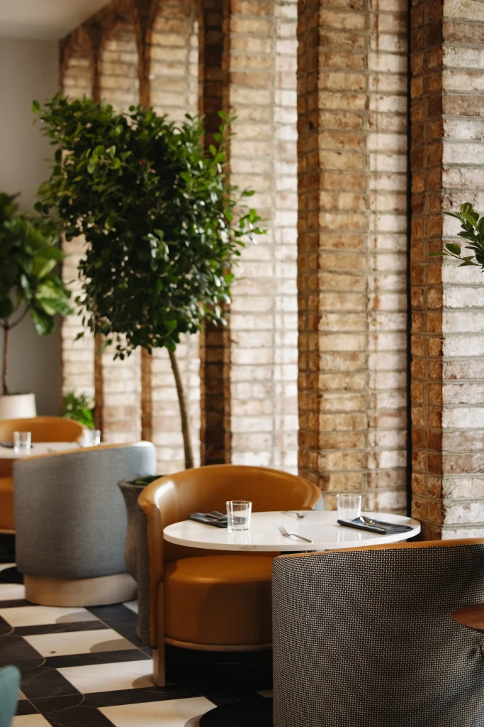 Esther's Table: Restaurant Interior Design, Minneapolis 11 Round cafe table with leather and woven barrel chairs beside original brick arches and a potted tree
